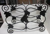 Front view of black metal wine rack showing scroll and leaf design