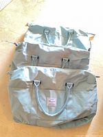 Three stacked light blue duffel bags showing exterior handles and brand patch