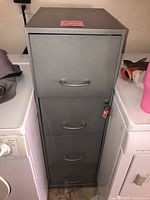 Front view of gray four-drawer metal file cabinet between appliances