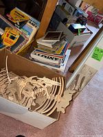 Box of plywood puzzle pieces, shelves and boxes of books, visible Crayola and Prang art supply boxes