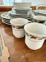 Stacked dinner plates, two mugs showing holly pattern and gold rim