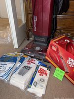 Group showing Hoover upright, Dirt Devil boxed handheld, three packs of vacuum bags