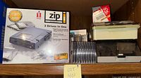 Boxed Iomega Zip 100 drive, stack of sealed Zip disks, plastic storage boxes