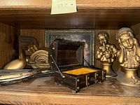 Shelf showing open wood chest, both J. Kendrick statues, musical wall plaques, floral painting