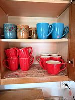 Cabinet shelves with assorted mugs: patterned tan/teal, blue, red stacks