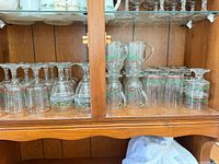 Cabinet shelf showing multiple styles of holly-band glassware including mugs, tumblers and stemware