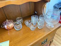 Wide view of all items on shelf: copper pot, tumblers, sherbet bowls, snifters, carafe