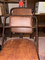 Front view of stacked brown metal folding chairs showing padded vinyl seats, backs and frame wear
