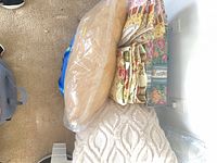 Bedspread folded with round tan pillow and square chenille pillow in plastic