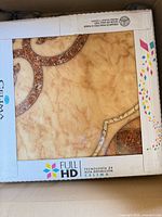 Close-up of tile showing beige marble look and brown medallion, branded packaging visible