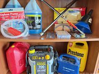Shelf view showing washer fluid jugs, siphon pump, lug wrench, funnel set, blue funnel, fuse pack, Stanley jump starter, red gas can, Westinghouse unit, yellow Prestone jug