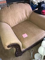 Front view of tan upholstered armchair with carved wood trim and seat cushion