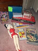 All items together showing board games stack, plush doll, VHS tape, comic