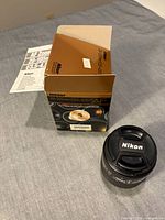 Lens with retail box and leaflet, cap nearby