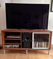 Front view of IKEA TV stand with TV on top showing shelving, centre compartment, sliding glass door