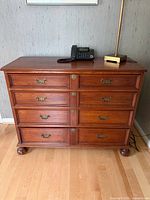 Full front view of solid wood dresser showing eight drawers, bun feet, lamp and phone on top
