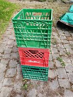Stacked view of two green and one red plastic milk crates showing colors, logo, and wear