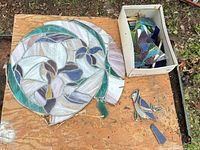 Two circular stained glass mosaics, small bird figure, box of glass shards on board