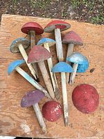 Group of painted wooden mushroom ornaments in red, blue and purple with varying stem conditions laid on wood surface