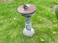 Full view of metal sundial on cement pedestal standing on grass