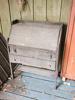 Front view of oak drop-front desk showing slanted writing surface, brass pulls, lower drawer, legs and stretcher