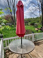 Round glass patio table with folded umbrella on deck