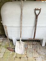 Group view of shovel, pitchfork and sledgehammer leaning against tank