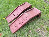 Pair of red perforated steel car ramps on grass