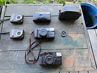 Six items on table: four cameras, case, lens cap