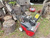 Left side profile of Yard Machines red/black snow blower near cut logs