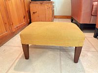 Overall view of yellow upholstered footstool with wooden legs