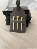 Front of tag showing three wooden tees inserted in pocket, stacked black boxes behind
