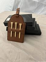 Stack of black boxes with one rawhide golf tag displaying four wooden tees