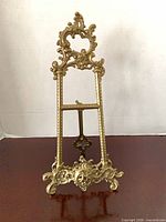 Front view of ornate brass easel stand showing scrollwork and resting ledge
