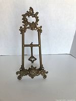 Front view of ornate brass easel stand showing scrollwork and shelf bar