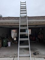 Full view of ladder extended against garage showing overall length and two-section structure