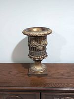 Front view of gilt resin urn on pedestal base