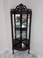 Full view of corner curio cabinet showing carved crest, glass panels, mirrored back, three shelves