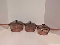 Front view of all three Corning Visions amber saucepans with lids