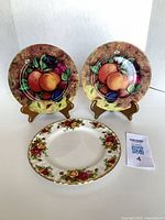 Two Email de Limoges fruit plates on stands and one Royal Albert Old Country Roses plate