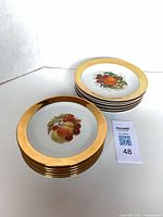 Stacked and spread view of six Fisher-China fruit motif plates showing gold rims