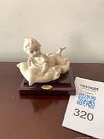 Front angled view of porcelain infant figurine on wood base with brass nameplate