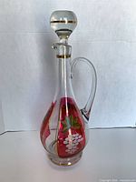 Front view of clear glass decanter with cranberry panels, enamel grape motif, stopper in place