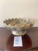 Side view of footed beige bowl showing blue floral design and gold rim