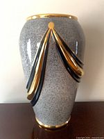 Front view of speckled gray ceramic floor vase with black and gold draped bands and gold rim