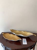 both ceramic leaf trays on table showing size comparison and gold interiors