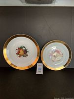 Front view of both plates showing size difference, gold rims and fruit motifs