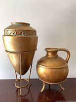 Tall and squat gold painted vessels on metal stands