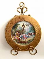 Front view of porcelain plate on gold-tone stand showing painted scene and gilt border