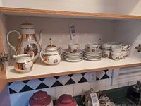 Full view of porcelain service on shelf showing pot, sugar, creamer, stack of saucers and cups